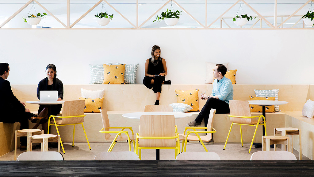 A group of people sitting in a room with yellow chairs and a table.