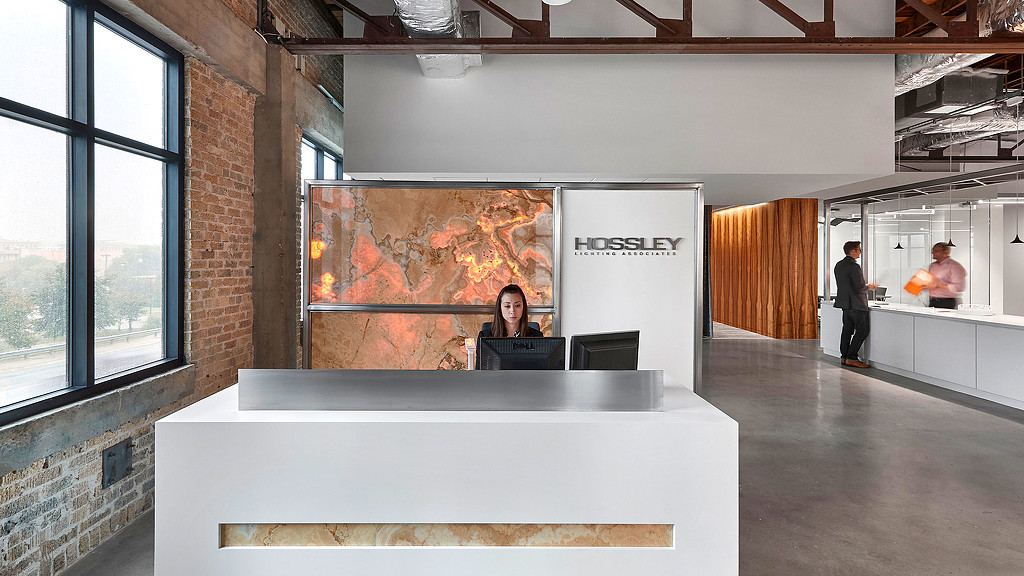 A person sitting at a desk in a room with a large screen.