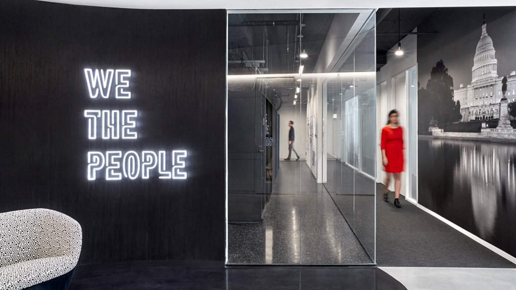 A person in a red dress walking down a hall with a sign.