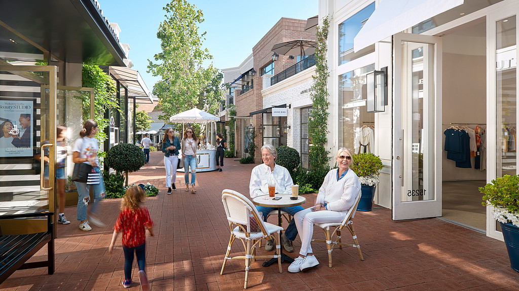 A person and a child sitting at a table outside a building.