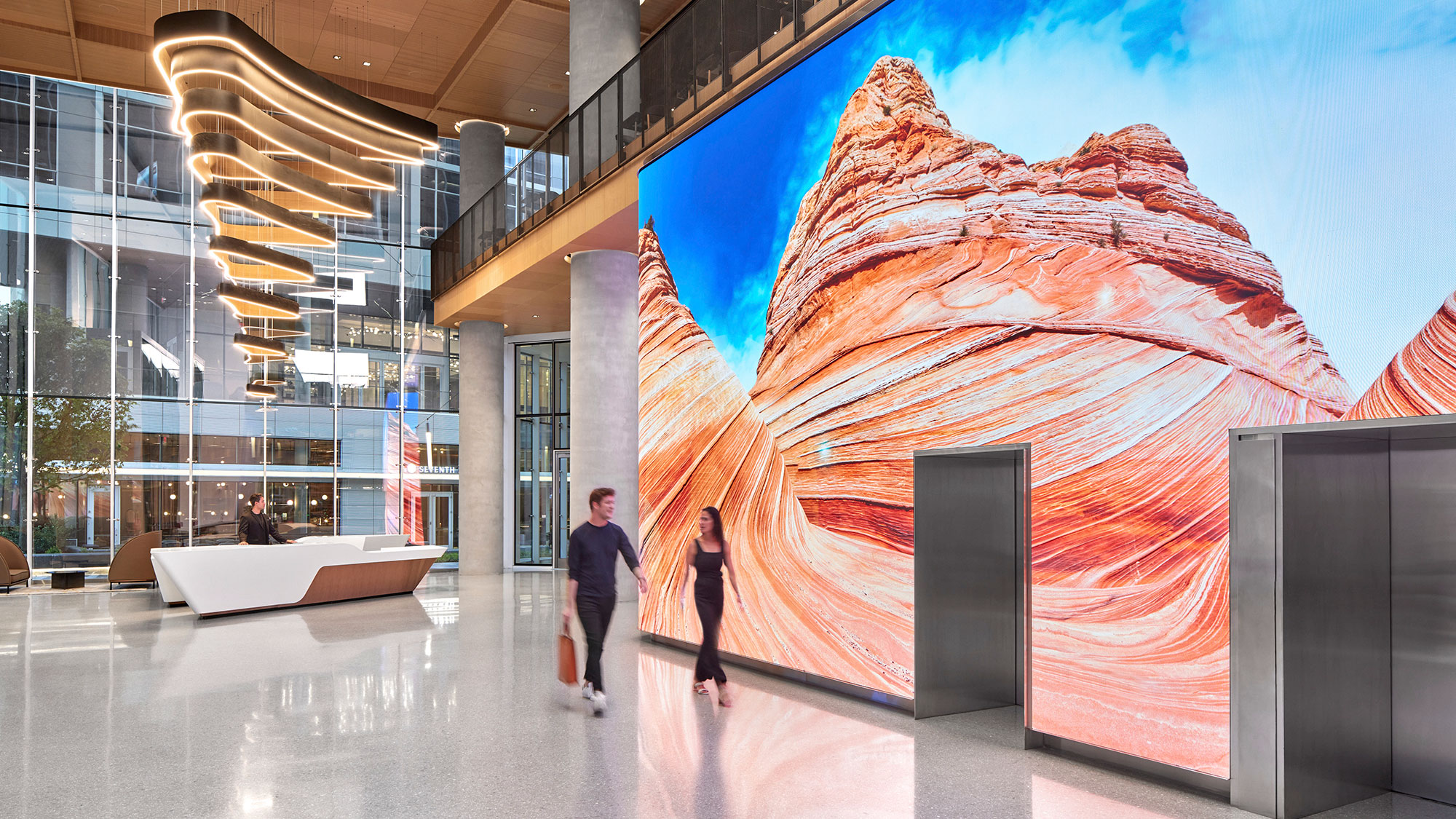 A man and woman walking in a building near a large digital wall.