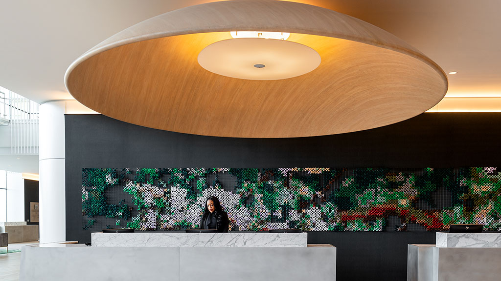 A person sitting on a ledge in front of a large wall with plants.