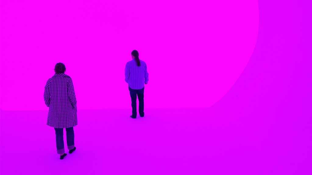 A woman and man standing in front of a hot pink James Turrell exhibit